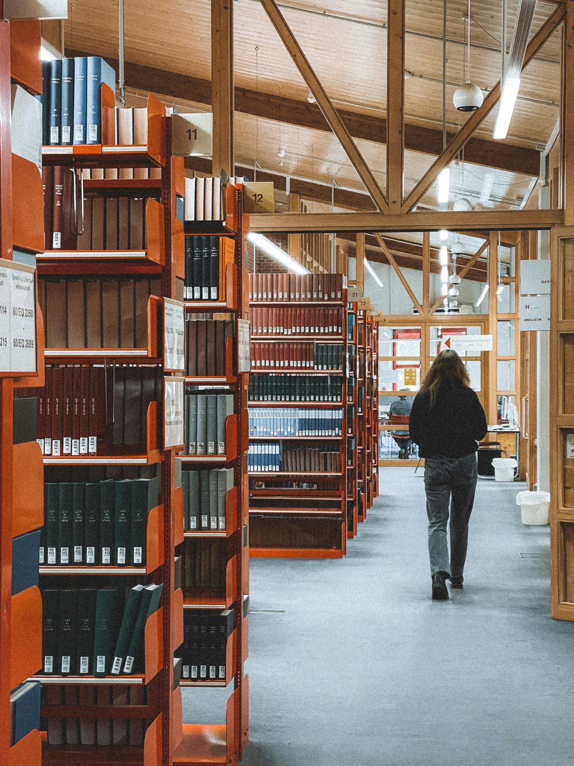 A person walking through a library in Germany, surrounded by bookshelves filled with literature.