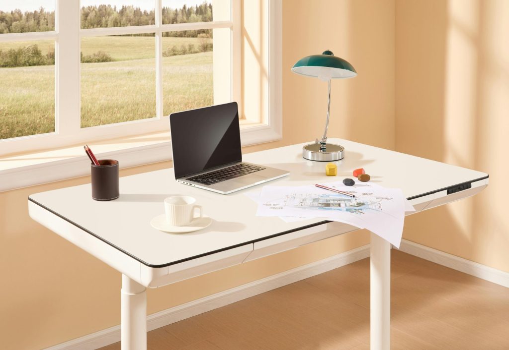 A bright modern home office with an adjustable desk, laptop, desk lamp, and design sketches by the window.